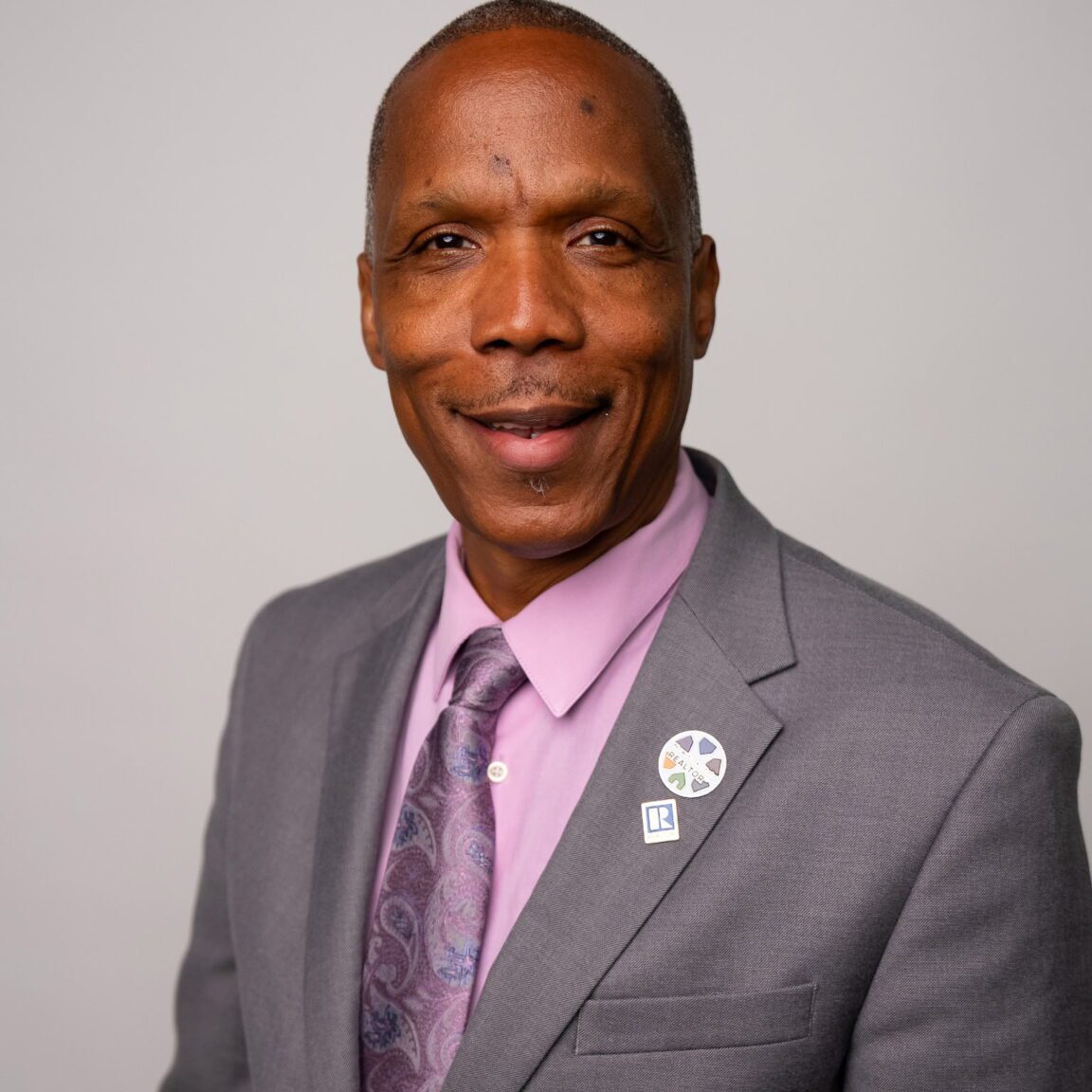 Professional portrait of a man in a gray suit and purple tie.